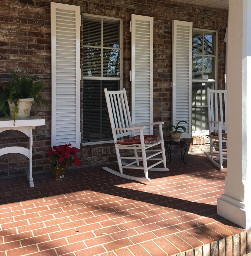 Front porch of a house with white Colonial shutters on the windows.